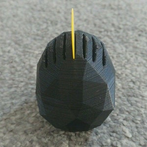 May include: A black, 3D printed, geometric object with a yellow plastic spike on top.