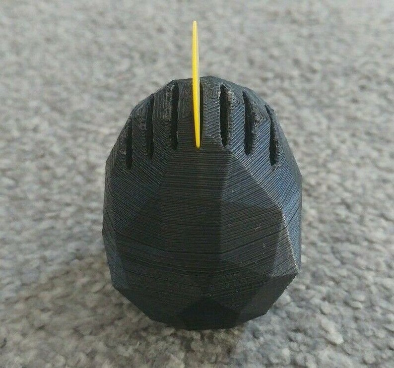 May include: A black, 3D printed, geometric object with a yellow plastic spike on top.