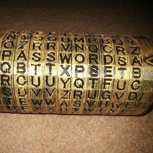 May include: A gold-coloured cylinder with multiple rotating rings, each ring displaying a different letter of the alphabet. The rings are labelled with the words "PASSWORD", "WORDS", "SET", and "ABC".