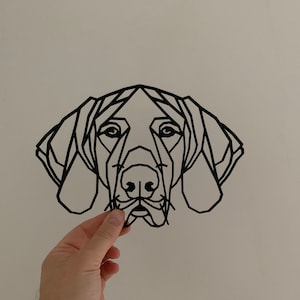 May include: Black geometric dog head wall art. The artwork features a stylized, low-poly design of a dog's face, with angular lines defining the features. The dog's eyes, nose, and ears are clearly visible in the minimalist design. The art is held by a hand.