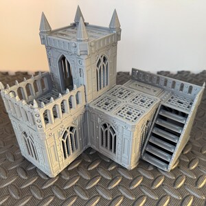 May include: A grey, 3D-printed miniature building with a castle-like design. The model features multiple levels, arched windows, and a staircase. The structure has a textured surface and is designed for tabletop gaming.