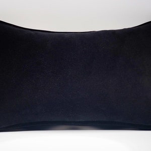 May include: A black velvet pillow with a simple, rectangular shape. The pillow is soft and plush, with a smooth, even surface.
