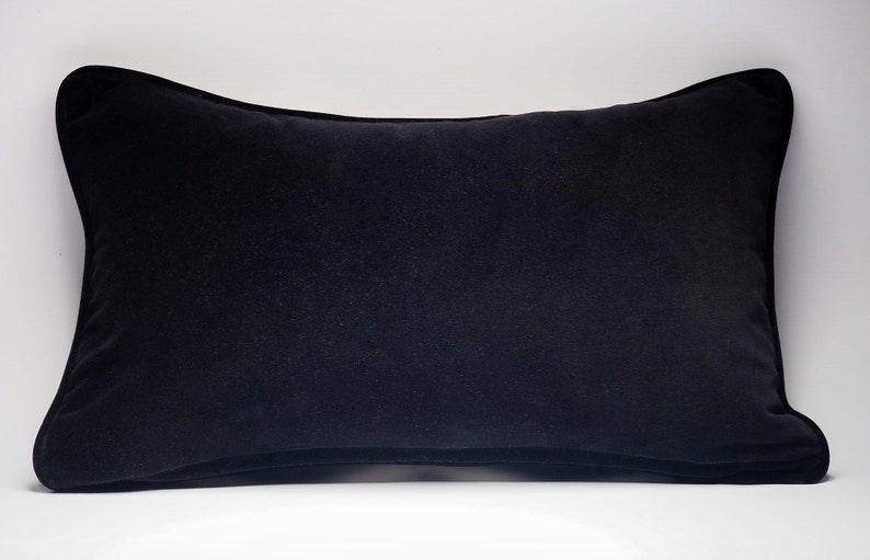 May include: A black velvet pillow with a simple, rectangular shape. The pillow is soft and plush, with a smooth, even surface.