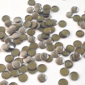 May include: A scattering of silver-toned metal embellishments with a green-gold center. The embellishments are round and have a slightly raised edge.