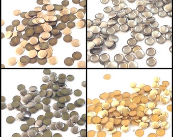 May include: Assortment of round metal embellishments in gold, silver, and bronze colors. The embellishments are scattered on a white background.