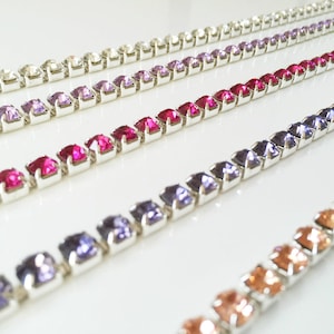 May include: Five rows of silver chains with square-shaped rhinestones in different colours. The colours are peach, purple, blue, pink, and clear.
