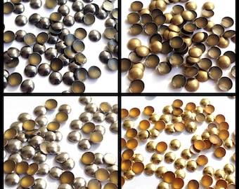 May include: Assortment of round metal embellishments in silver and gold colors. The embellishments are scattered on a white background.