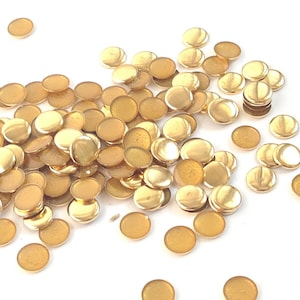 May include: A large pile of gold-colored metal round embellishments. The embellishments are scattered on a white surface.