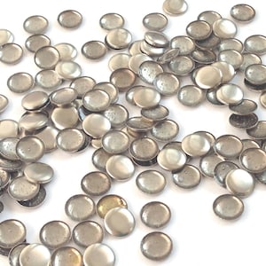 May include: A large quantity of silver-colored metal round embellishments. The embellishments are scattered on a white surface.