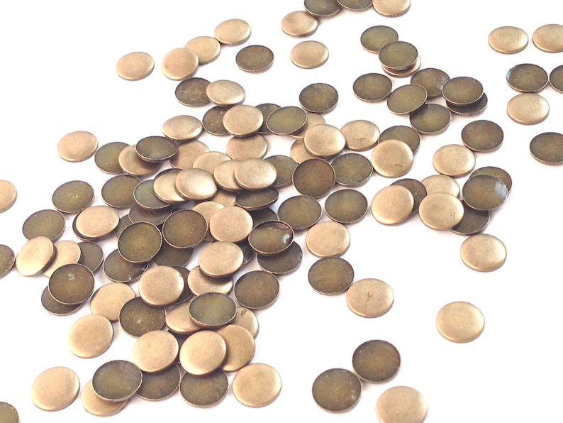 May include: A pile of round, flat, brass-colored metal discs. The discs are scattered on a white surface.