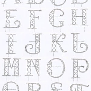 May include: A set of 26 silver rhinestone alphabet cake toppers. Each letter is made of a silver wire frame with rhinestones. The letters are on a silver wire pick.