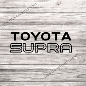 May include: Black text on a light gray wood grain background reads "TOYOTA SUPRA". The word "TOYOTA" is in a bold, sans-serif font, while "SUPRA" is in a outlined, sans-serif font.