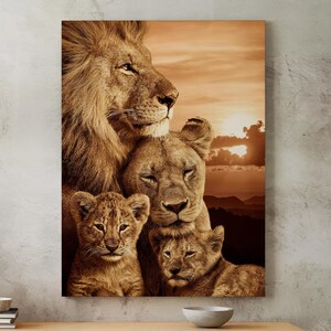 Könnte beinhalten: Ein Leinwanddruck mit einer Löwenfamilie. Die Löwin und zwei Junge kuscheln sich aneinander, während der männliche Löwe hinter ihnen steht. Der Hintergrund ist ein Sonnenuntergang mit einer Bergkette in der Ferne.