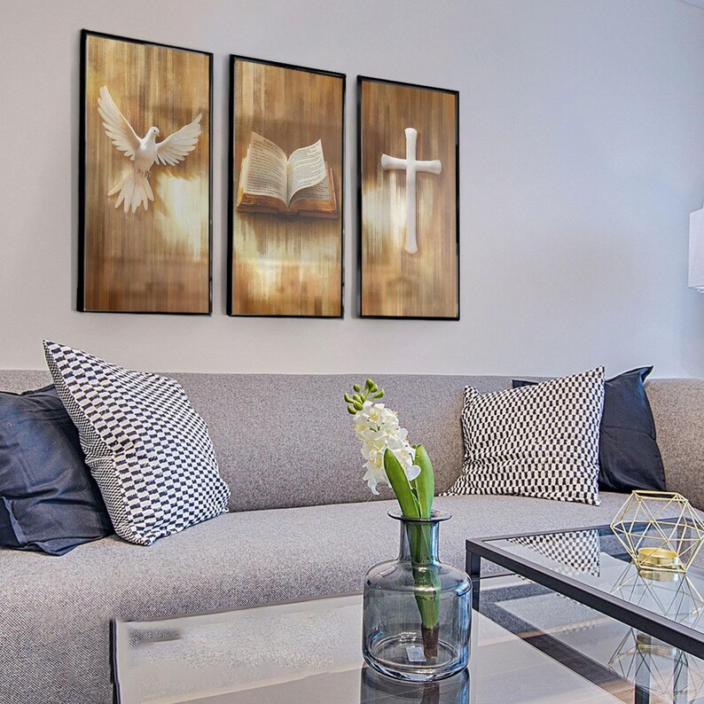 K&ouml;nnte beinhalten: Ein Triptychon gerahmter Wandkunst mit religi&ouml;sen Symbolen. Die Tafeln zeigen eine wei&szlig;e Taube, ein offenes Buch und ein Kreuz, alle vor einem strukturierten Hintergrund in Holzoptik. Das Kunstwerk wird &uuml;ber einem grauen Sofa mit dekorativen Kissen pr&auml;sentiert.