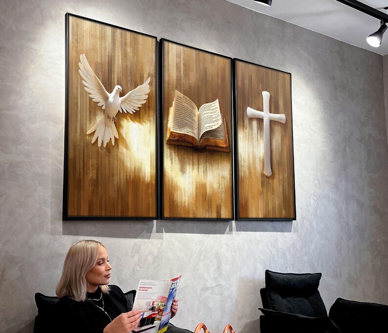 K&ouml;nnte beinhalten: Ein Triptychon aus gerahmten Kunstpaneelen mit religi&ouml;sen Symbolen. Die Paneele zeigen eine wei&szlig;e Taube, ein offenes Buch und ein Kreuz, alles vor einem strukturierten, holzfarbenen Hintergrund. Das Kunstwerk ist in Schwarz gerahmt.