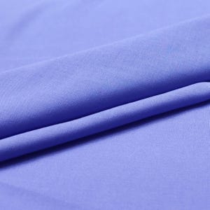 Puede incluir: Primer plano de una tela doblada de color azul bígaro liso. La tela tiene una textura suave y está drapeada en pliegues suaves, creando sombras y profundidad.