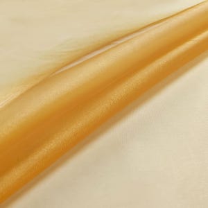 May include: A piece of sheer, translucent fabric in a vibrant golden-yellow hue. The material is draped to create soft, flowing folds, highlighting its lightweight, semi-transparent texture and smooth, slightly shimmering surface finish.