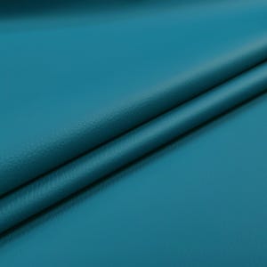 May include: Close-up of a teal-colored leather material with a subtle texture. The fabric is folded, creating diagonal lines and shadows. The color is a vibrant, saturated teal, with a slight sheen.