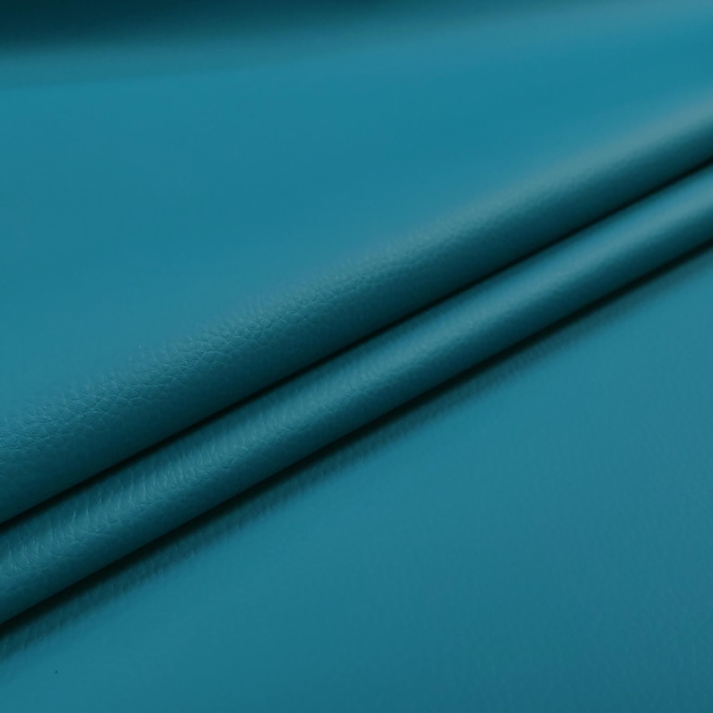 May include: Close-up of a teal-colored leather material with a subtle texture. The fabric is folded, creating diagonal lines and shadows. The color is a vibrant, saturated teal, with a slight sheen.