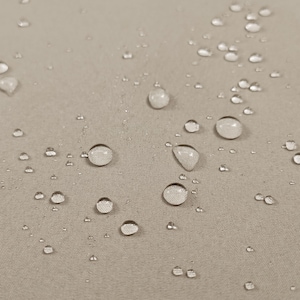 Puede incluir: Primer plano de una tela beige con numerosas gotas de agua dispersas. Las gotas varían en tamaño y reflejan la luz, creando una apariencia texturizada. La tela parece ser resistente al agua.