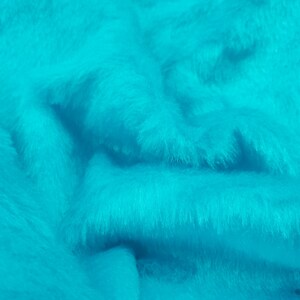May include: A vibrant turquoise faux fur fabric with a dense, soft, and shaggy texture. The material features deep folds and ripples that create natural shadows and highlights across the bright, saturated blue-green surface of the textile.