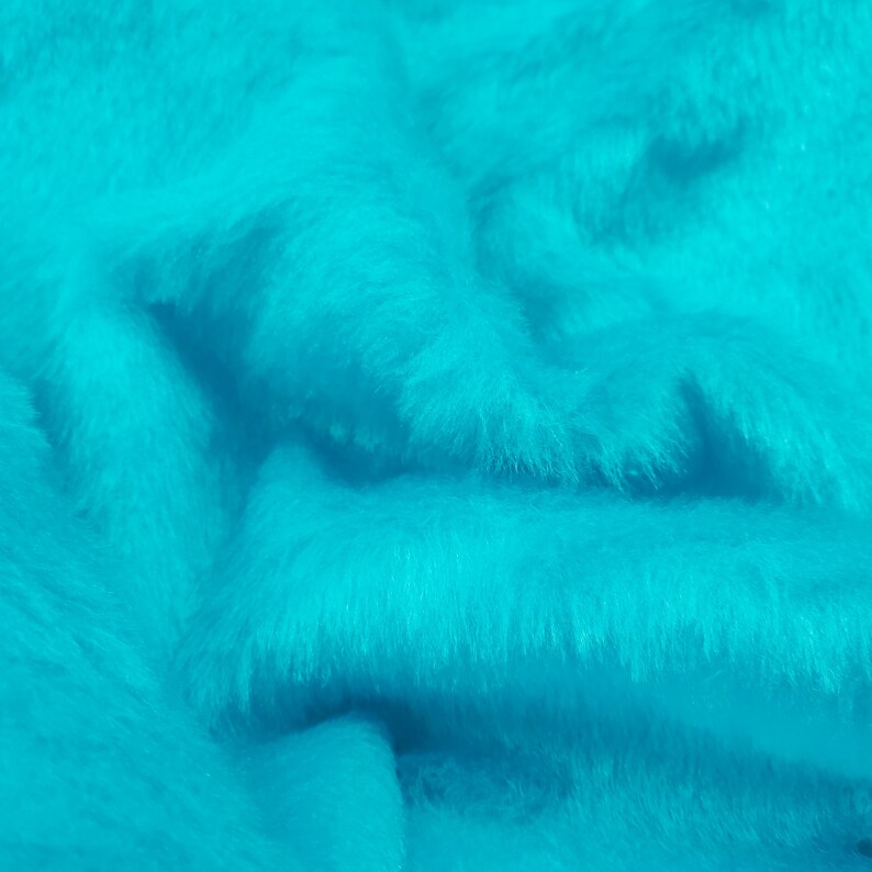 May include: A vibrant turquoise faux fur fabric with a dense, soft, and shaggy texture. The material features deep folds and ripples that create natural shadows and highlights across the bright, saturated blue-green surface of the textile.