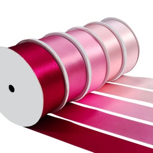 Può includere: Un rotolo di nastro di raso rosa e rosso, con il nastro che si svolge in un gradiente di colori dal rosso scuro al rosa chiaro.