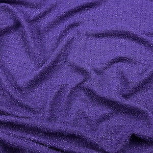 Op de afbeelding: Close-up van een dieppaarse stof met een getextureerde, geweven uitstraling. Het materiaal heeft een subtiele glans, met kleine vlekjes lichtere kleur verspreid. De stof is gedrapeerd, waardoor zachte plooien en schaduwen ontstaan.