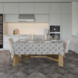 Könnte beinhalten: Ein Esstisch, der für eine Mahlzeit gedeckt ist. Der Tisch ist mit einer geometrisch gemusterten Tischdecke in Grau- und Weißtönen bedeckt. Der Tisch ist mit Tellern, Gläsern und Besteck gedeckt. Auf beiden Seiten des Tisches stehen zwei beige Stühle.