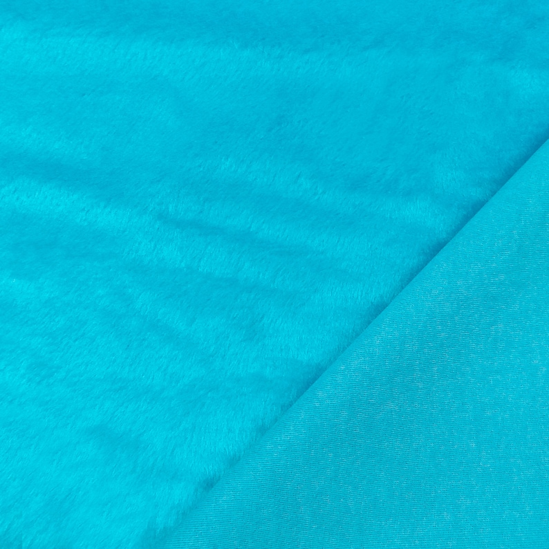 May include: A vibrant turquoise fabric featuring a plush, faux fur texture on one side and a smooth, solid-colored woven backing on the other. The material displays a consistent, bright blue-green hue across both the soft, fuzzy surface and the flat, matte underside, showcasing the contrast between the two distinct textile finishes.