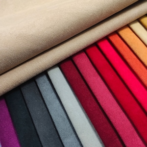 Op de afbeelding: Een verzameling stofstalen in verschillende kleuren, waaronder paars, zwart, grijs, blauw, rood, oranje en geel. De stalen zijn gerangschikt in een regenboogpatroon, met de lichtste kleur bovenaan en de donkerste kleur onderaan.