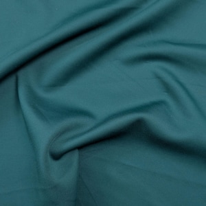 Könnte beinhalten: Nahaufnahme eines teal-farbenen Stoffes mit sanften Falten und subtilen Schatten. Der Stoff hat eine glatte Textur und eine satte, einfarbige Farbe, die ein Gefühl von Tiefe und Bewegung erzeugt. Das Material scheint ein mittelschweres Textil zu sein.