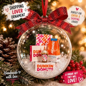 May include: A clear Christmas ornament with miniature Dunkin' Donuts products inside, including a coffee cup, boxes, and a bag of coffee. The ornament is decorated with a red bow and the text "SHOPPING LOVER ORNAMENT".