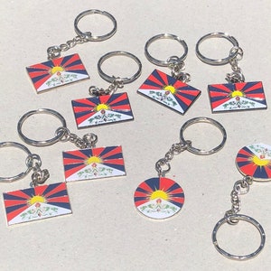 May include: A set of ten keychains featuring the Tibetan flag. Each keychain has a silver ring and a small metal charm with the flag design. The flags are red, blue, and yellow with a stylised sun in the centre.