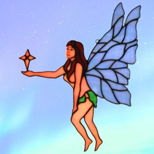May include: A stained glass fairy with blue wings holding a star. The fairy has long brown hair and is wearing a green skirt. The background is a light blue with white dots.