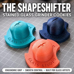 May include: Three 3D-printed stained glass grinder cookies in teal, dark blue, and orange. Each features a central dome with a bird icon and the text "GLASS STUDIO" embossed on the base. The text "THE SHAPESHIFTER STAINED GLASS GRINDER COOKIES" appears above.