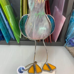 Pu&ograve; includere: Una scultura di gabbiano in vetro colorato con corpo perlato, ali turchesi e becco e zampe gialle. L'uccello &egrave; in piedi su una base di pietra bianca. La scultura ha sottili gambe di metallo e una piccola etichetta attaccata.