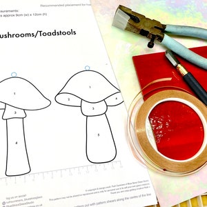 Op de afbeelding: Een zwart-witte lijntekening van twee paddenstoelvormen, genummerd van 1 tot en met 5. De tekening staat op een wit vel papier met een rasterpatroon. Het papier ligt naast een rol koperfolietape, een rood stuk glas en een glassnijder.