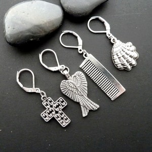 May include: Four silver charm earrings with different designs: a cross, angel wings, a comb, and a seashell.
