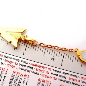 Op de afbeelding: Goudkleurige oorbel met een pijlvormige hanger. De hanger is verbonden met een ketting en een sluiting. De oorbel is ongeveer 3,8 cm lang.