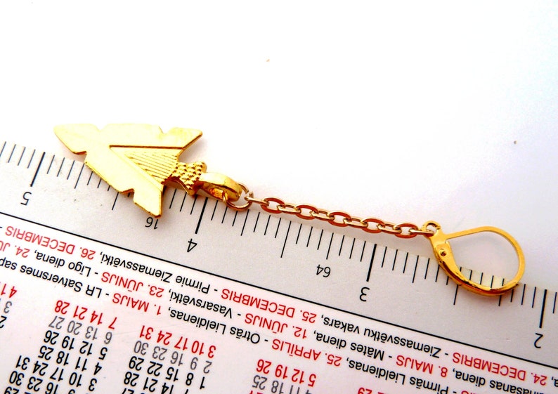 Op de afbeelding: Goudkleurige oorbel met een pijlvormige hanger. De hanger is verbonden met een ketting en een sluiting. De oorbel is ongeveer 3,8 cm lang.