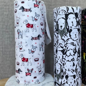 K&ouml;nnte beinhalten: Zwei Rollen wei&szlig;er Papierhandt&uuml;cher mit verschiedenen Hunde-Designs. Eine Rolle hat einen wei&szlig;en Hintergrund mit bunten Hunden, die Pullover und H&uuml;te tragen. Die andere Rolle hat ein Schwarzwei&szlig;-Design mit Hunden in verschiedenen Posen.
