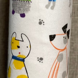 K&ouml;nnte beinhalten: Wei&szlig;er Papierhandtuchhalter mit einem bunten Muster aus Hunden. Die Hunde sind grau, gelb, orange und blau mit schwarzen Flecken. Der Hintergrund ist wei&szlig; mit grauen Pfotenabdr&uuml;cken.