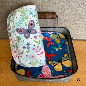 May include: A galvanized metal tray with a wooden handle containing several round fabric cloths. One cloth features a light blue background with colorful butterflies and floral patterns, while others inside the tray display a dark blue background with red, yellow, and orange butterflies.