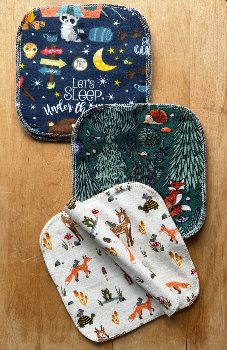 May include: Three square fabric cloths with different woodland-themed prints. The top cloth is navy blue with white stars, a moon, and the text "Let's Sleep Under the Stars". The middle cloth is green with a large tree, mushrooms, and a fox. The bottom cloth is white with a repeating pattern of deer, foxes, mushrooms, and turtles.