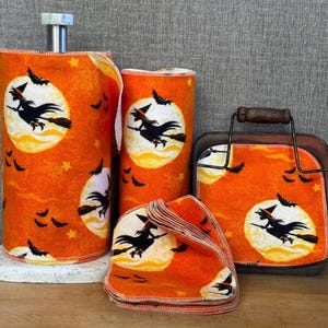 May include: A set of reusable fabric towels and cloths featuring an orange background with a repeating pattern of black silhouettes of witches flying on broomsticks against yellow full moons, accented by small black bats and stars.