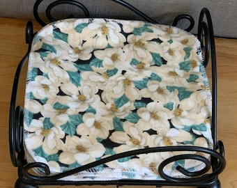 May include: A black metal napkin holder with a floral design. The napkin holder is filled with white napkins with a floral pattern.