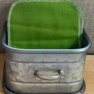 May include: A galvanized metal planter with a handle, filled with a stack of green fabric squares.