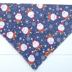 May include: A blue bandana with a repeating pattern of Santa Claus figures and snowflakes. The bandana has a brown leather tag with the word "Charming" printed on it.