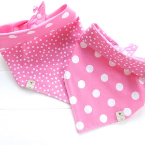 May include: Two pink fabric dog bandanas with white polka dots. One bandana has small white polka dots and the other has large white polka dots. Both bandanas have a small brown leather tag with the word "Doggy" on it.